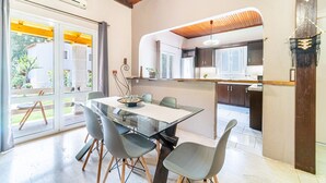 Een moderne keuken met een glazen eettafel en stoelen, houten balkenplafond en uitzicht door de glazen deuren.