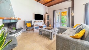 Een woonkamer met een open haard, een bank, een salontafel en een aan de muur bevestigde televisie.
