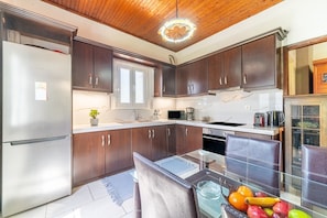 A kitchen with dark wooden cabinets, stainless steel appliances, a glass dining table, and a fruit bowl.
