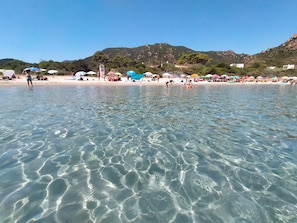 Ein Strand mit klarem Wasser, Sonnenschirmen und Menschen.