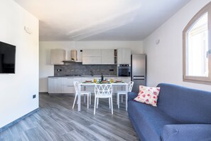 Een moderne keuken met witte kasten, een eettafel met stoelen en een blauwe bank met een decoratief kussen.