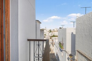 A narrow street with white buildings, a metal gate, and a clear sky.
