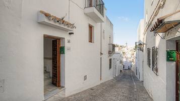 Une ruelle étroite pavée, bordée de bâtiments blancs dotés de balcons et de portes.