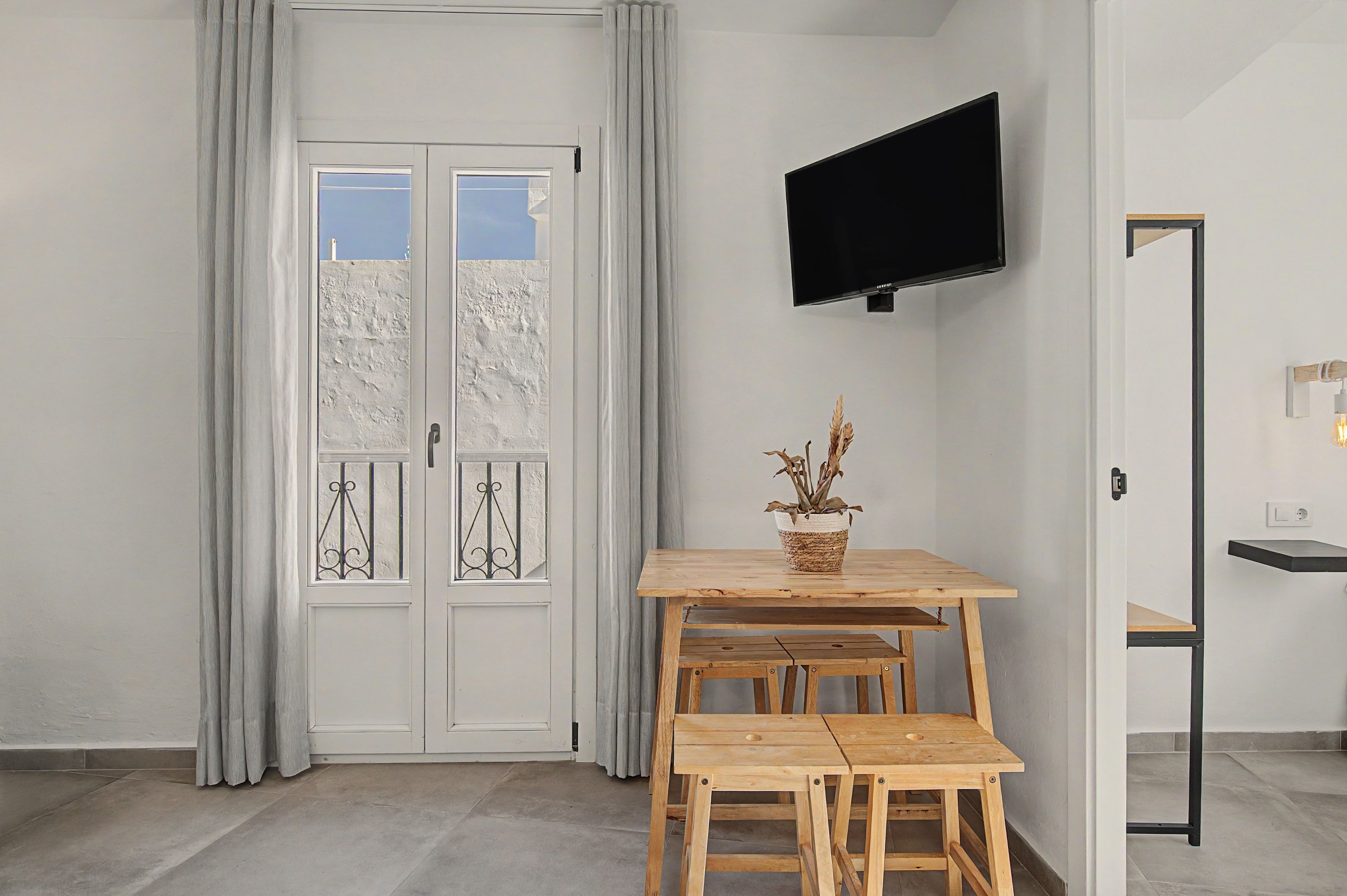 A room with a wooden table and benches, a flat-screen TV mounted on the wall, a potted plant, and a door with a window.