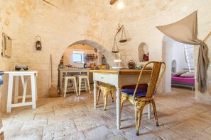 A rustic stone-walled room with a wooden desk, a chair, and a small table.