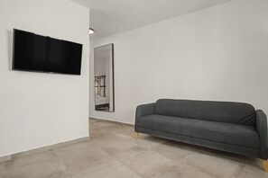 A modern living room with a flat-screen TV mounted on the wall, a large mirror, and a grey sofa.