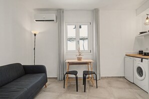 A compact living space with a sofa, a small table with two chairs, a washing machine, and a floor lamp.