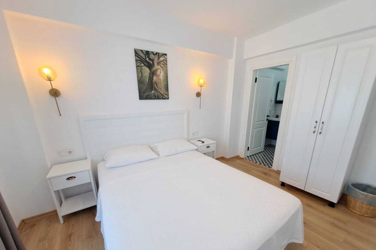 A bedroom with a bed, bedside tables, a wardrobe, and two wall-mounted lamps.