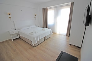 A clean, modern hotel room with a large bed, bedside tables, a flat-screen TV, and a large window with curtains.