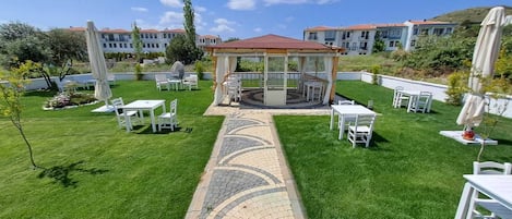 A gazebo with a tiled pathway leading to it, surrounded by white tables and chairs.