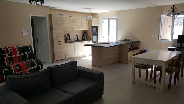 Eine moderne Küche mit Holzausstattung, ein Essbereich mit weißem Tisch und Stühlen sowie ein graues Sofa im Wohnzimmer.
