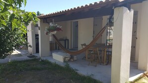 Eine überdachte Terrasse mit einer Hängematte, Holzmöbeln und einer hängenden Blumenkomposition.
