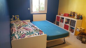 Ein Schlafzimmer mit einem Bett, einem Fenster, einem Bücherregal und einer Spielzeugkiste.