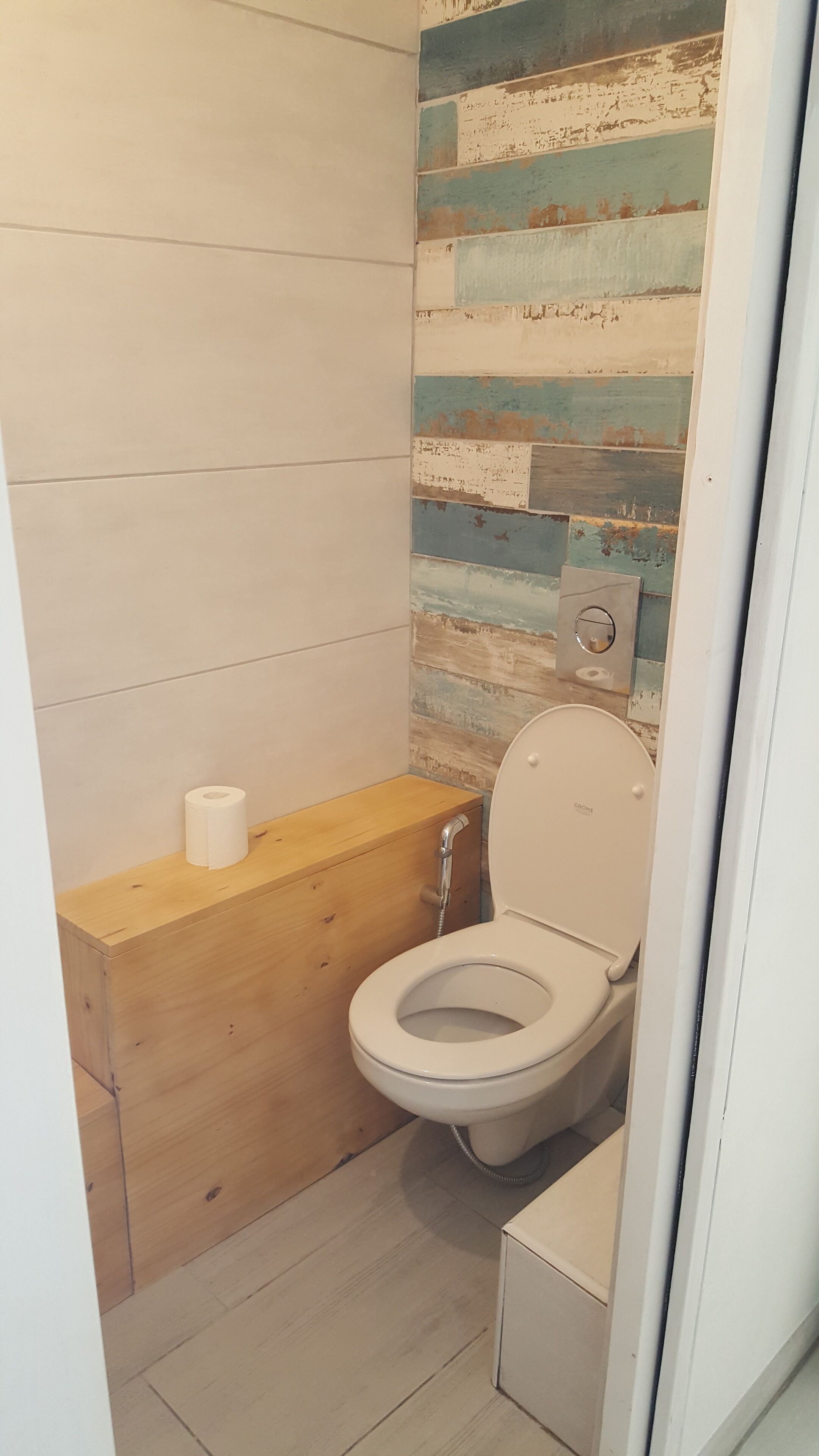 A small bathroom with a wooden vanity, a toilet, and a wall with a distressed wood panel design.