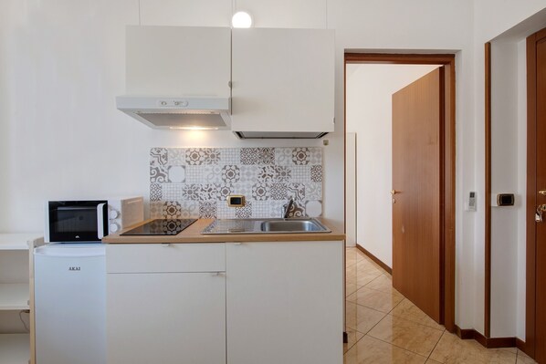 A compact kitchen with a microwave, a small refrigerator, a sink, and a patterned backsplash.