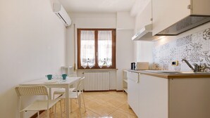 Eine kleine Küche mit Esstisch, Stühlen, einem Fenster mit Vorhängen, einem Heizkörper und einer gefliesten Spritzschutzwand.