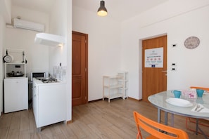 A compact kitchen with a stove, microwave, and white cabinets. There is a dining area with a glass table and orange chairs.