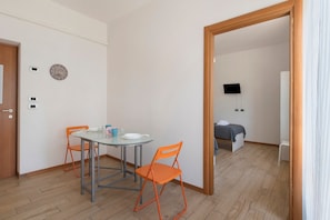 A room with a bed, a TV, a table with chairs, and a door.