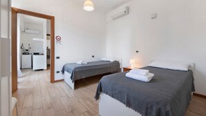A hotel room with two beds, a kitchenette, a bathroom, and a door leading to another room. - Apartment Civico22 - Bilo 3 with Balcony, A/C & Wi-Fi (Peschiera del Garda)