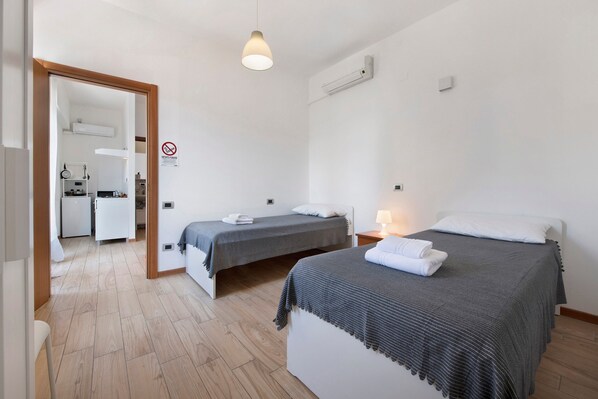 A hotel room with two beds, a kitchenette, a bathroom, and a door leading to another room.