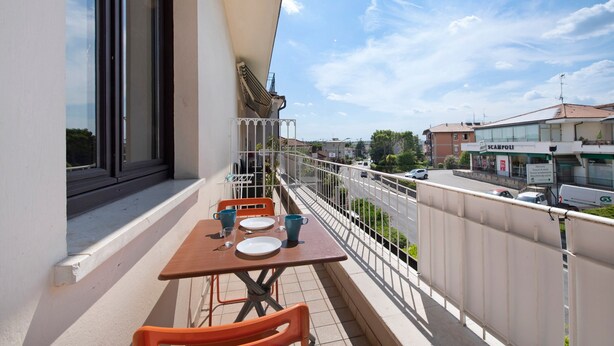 A balcony with a table and chairs, a railing, and a view of the street and buildings. - Apartment Civico22 - Bilo 3 with Balcony, A/C & Wi-Fi (Peschiera del Garda)