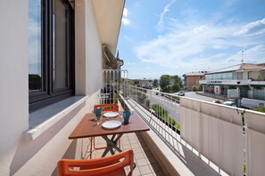 A balcony with a table and chairs, a railing, and a view of the street and buildings.