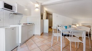 A compact kitchen with white appliances, a dining area with white chairs, and a visible doorway leading to another room.