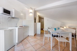 A compact kitchen with white appliances, a dining area with white chairs, and a visible doorway leading to another room.