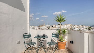 A balcony with two chairs and a table, a potted plant, and a view of a white-walled town.