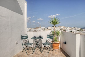 A balcony with two chairs and a table, a potted plant, and a view of a white-walled town.