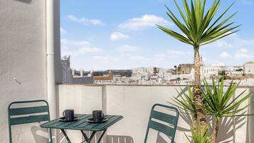 A balcony with two green chairs, a small table with two black cups, and a tall palm plant.