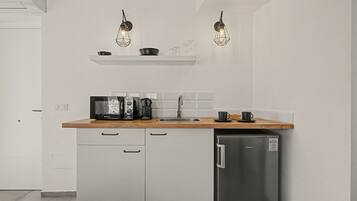 A modern kitchen with white cabinetry, a wooden countertop, a stainless steel refrigerator, and two pendant lights.