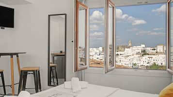 Una habitación de hotel con cama, escritorio, silla, televisor y ventana con vista a la ciudad.