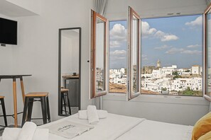 Quarto de hotel com cama, escrivaninha, cadeira, televisão e janela com vista para a cidade.