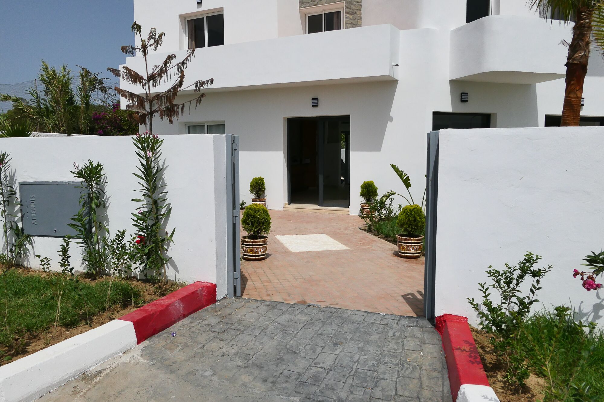 A modern building with a central entrance, potted plants, and a paved pathway leading to the entrance.