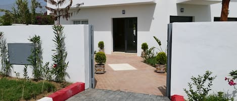 A modern building with a central entrance, potted plants, and a paved pathway leading to the entrance.