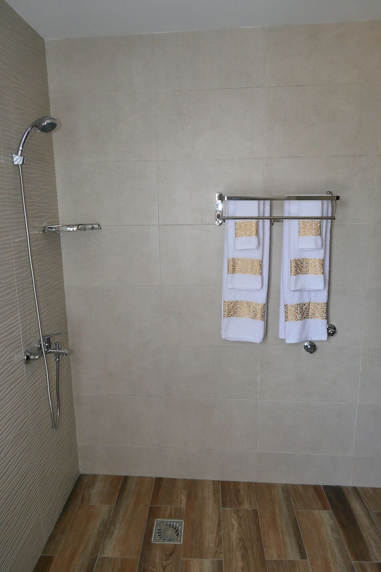 Un baño con ducha, dos toallas en un perchero y suelo de madera.