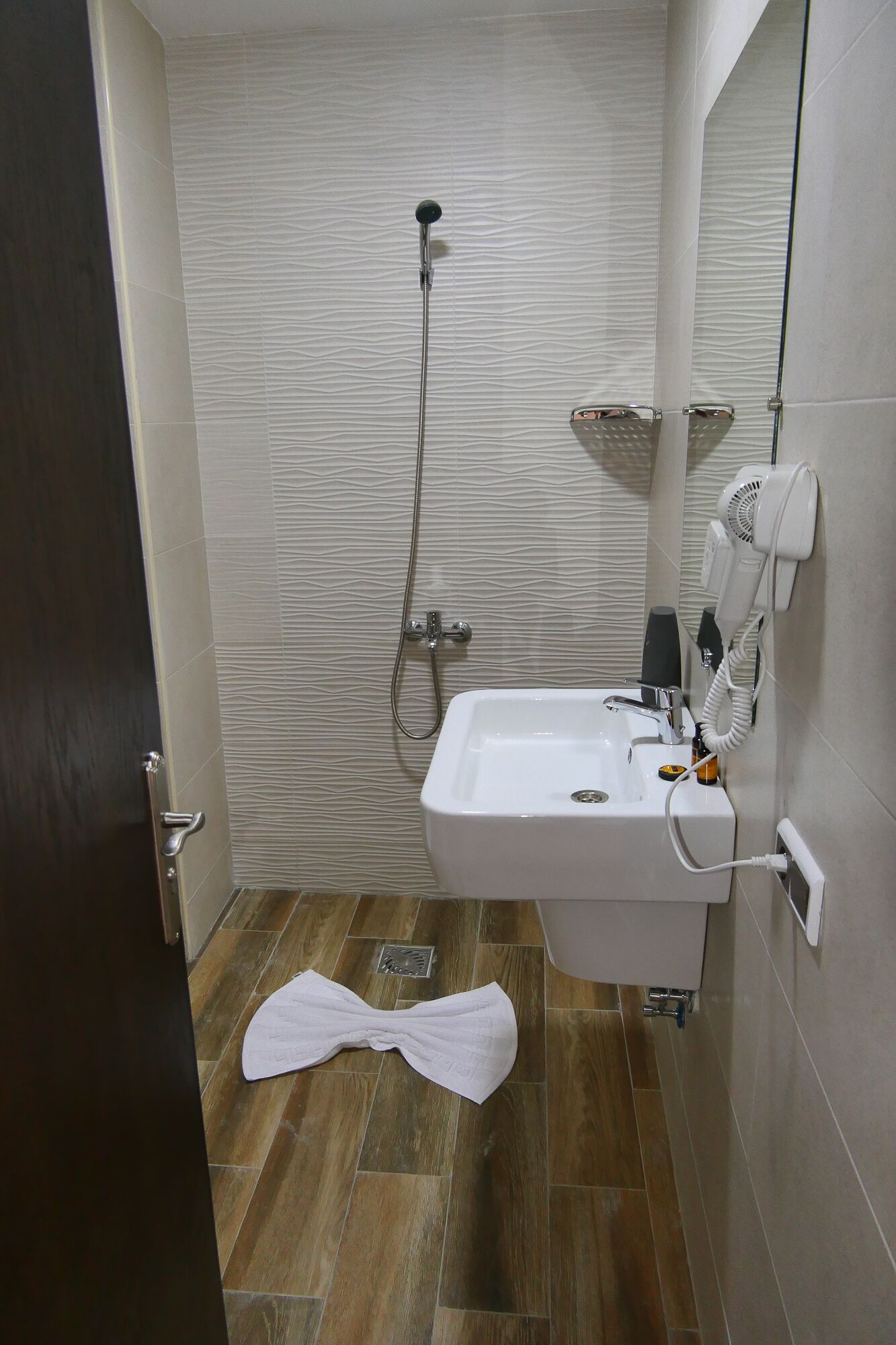 Ein Badezimmer mit einem weißen Waschbecken, einer Handbrause, einem Handtuch auf dem Boden und einem Föhn an der Wand.