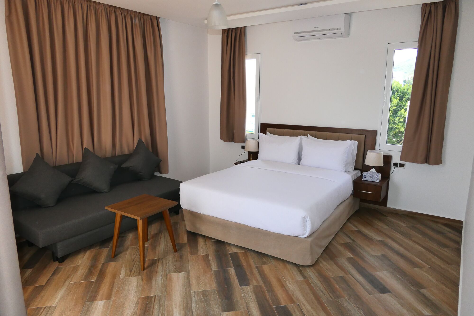 A hotel room with a bed, a sofa, a small table, and a nightstand with lamps.