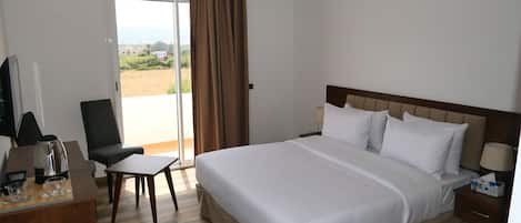 Habitación de hotel con cama, escritorio, silla, televisor y ventana con cortinas.