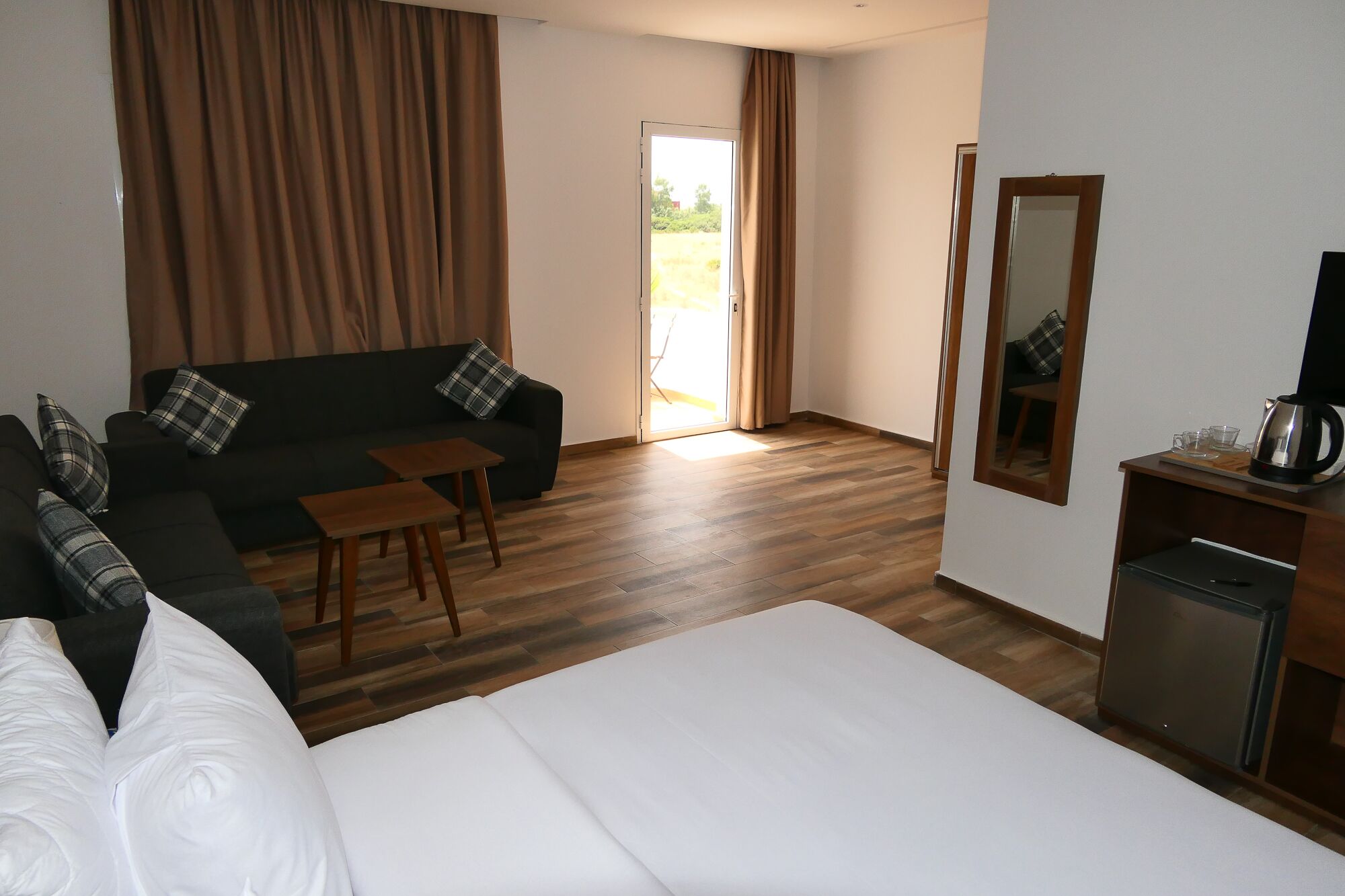 A hotel room with a bed, a sofa, a small table, a mirror, and a coffee maker.