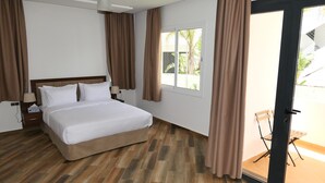 Una habitación de hotel con una cama, una mesita de noche, una lámpara y una puerta corrediza de vidrio que da a un espacio exterior.