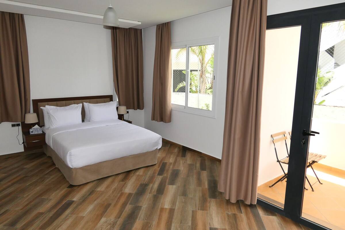 A hotel room with a bed, a nightstand, a lamp, and a sliding glass door leading to an outdoor area.