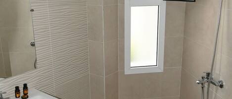 Un baño con lavamanos, espejo, ducha y ventana.