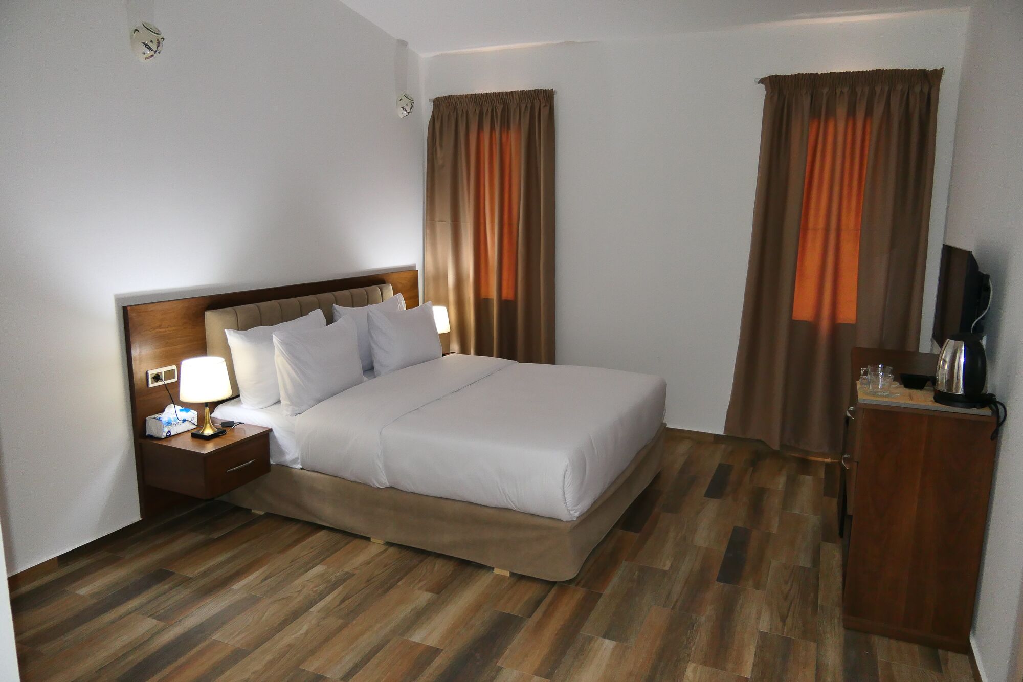 Una habitación de hotel con cama, mesita de noche, lámpara, cortinas y televisor.