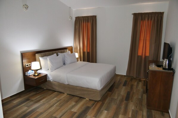 Una habitación de hotel con cama, mesita de noche, lámpara, cortinas y televisor.
