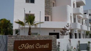 Un hotel de varios pisos con fachada blanca, detalles de piedra y un letrero que dice 'Hotel Corail'.