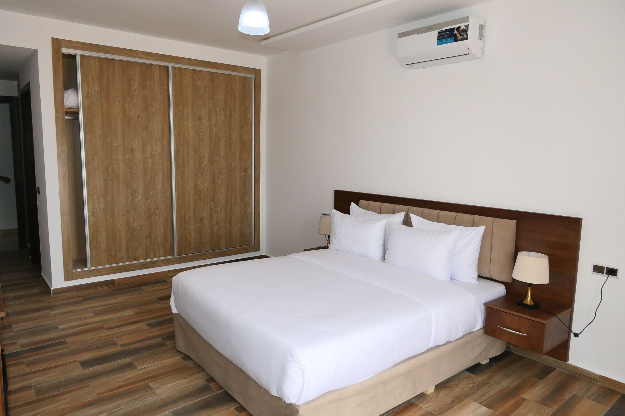 Una habitación de hotel con una cama grande, armario de madera, lámparas de noche y un equipo de aire acondicionado.