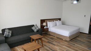 Una habitación de hotel con cama, sofá, una mesita y un mueble auxiliar.