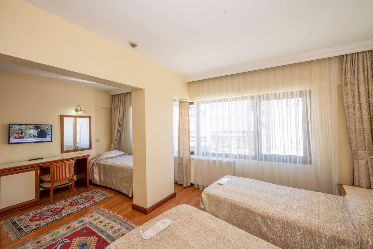 Une chambre d’hôtel avec deux lits, un bureau, une télévision et une grande fenêtre avec des rideaux.